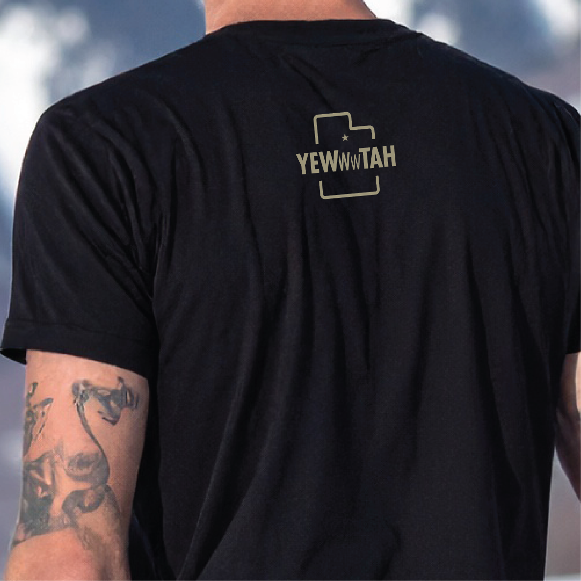 Black t-shirt with 'YEWWWTAH' logo on the back, worn by a person with tattoos.