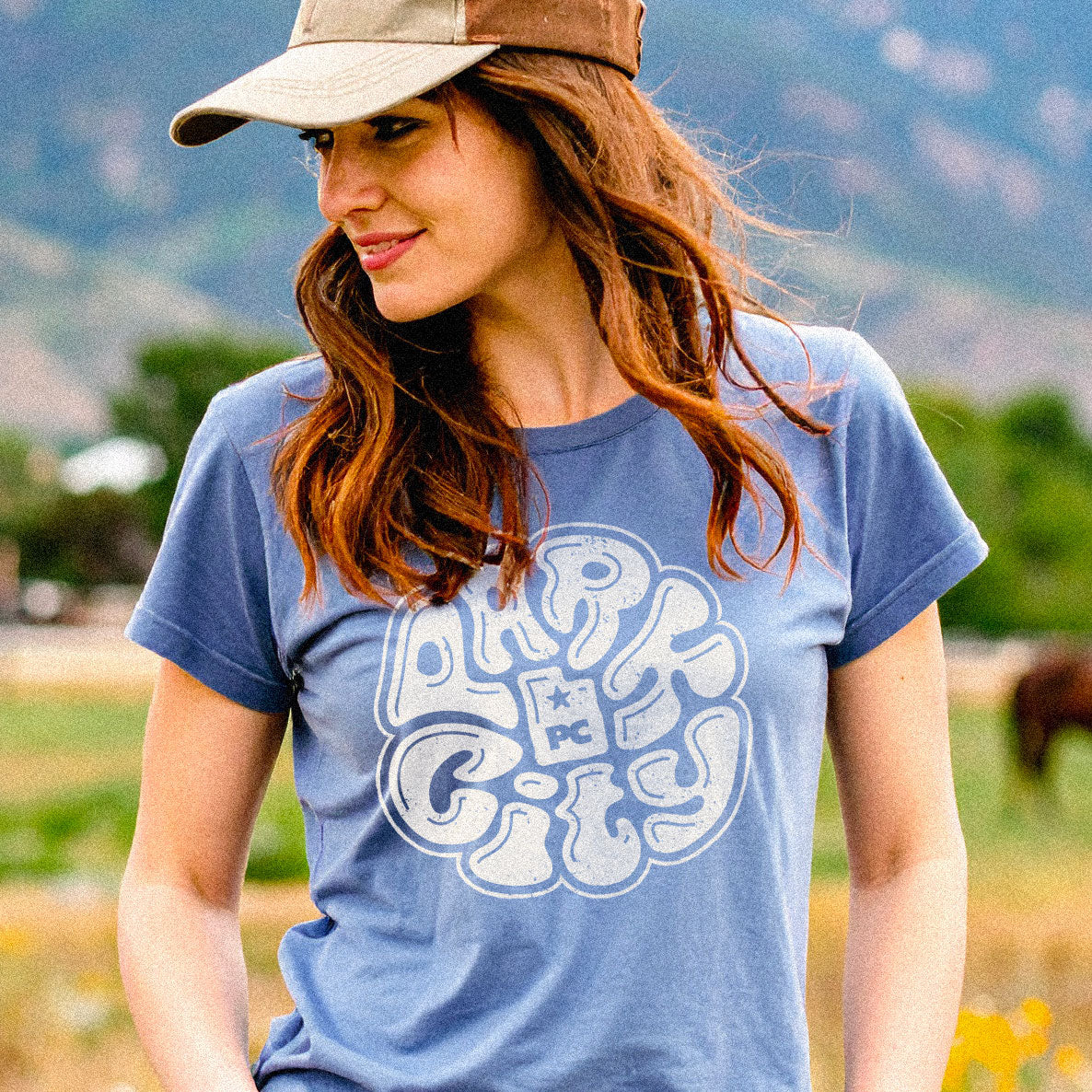 Woman wearing a blue t-shirt with 'Park City' graphic in a natural setting