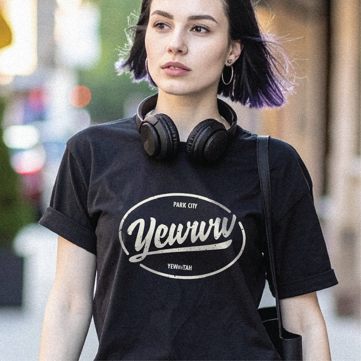 Woman wearing a black t-shirt with an ovular 'Yewww' logo, standing outdoors.