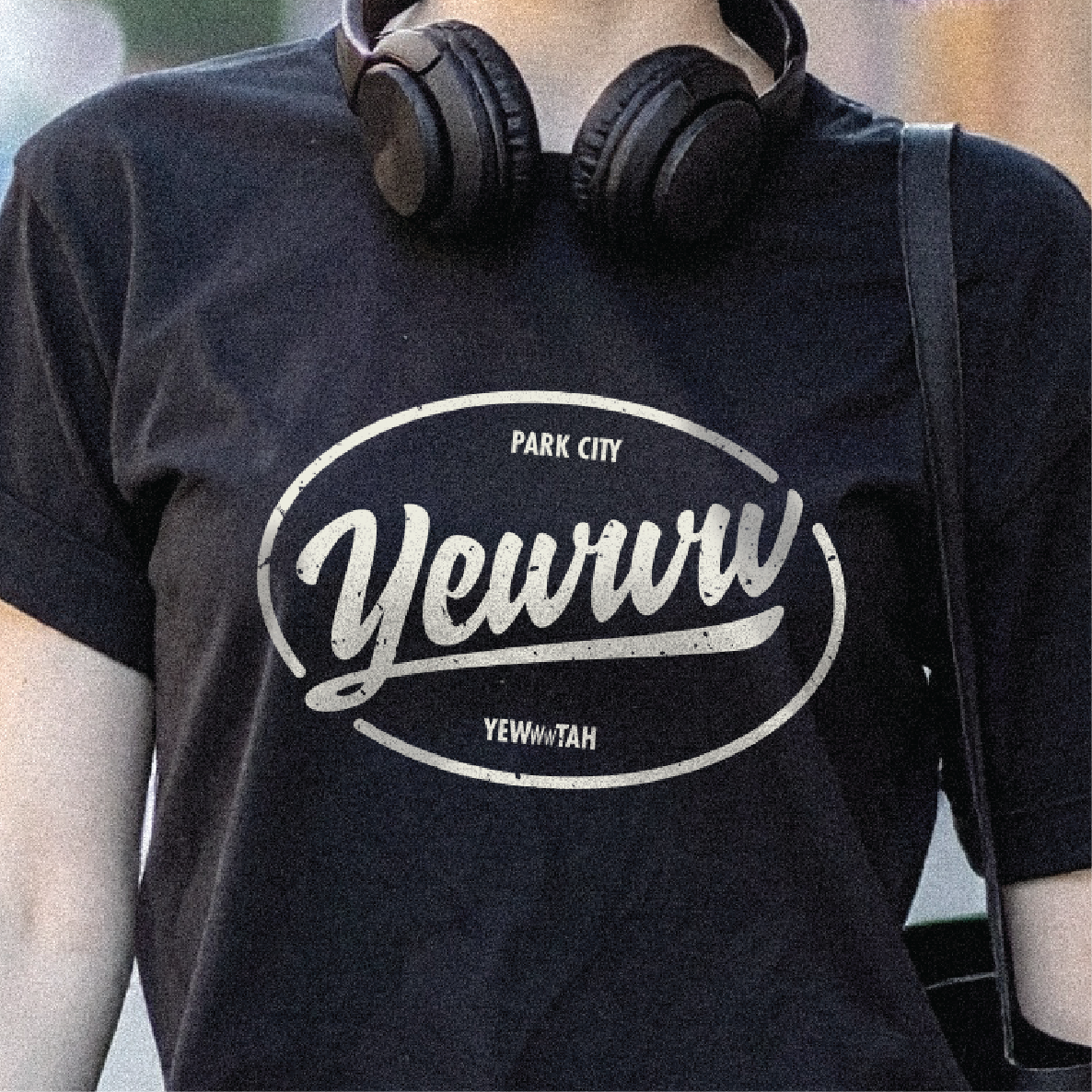 Person wearing a black t-shirt with oval 'Yewww' logo and Park City text, standing outdoors.