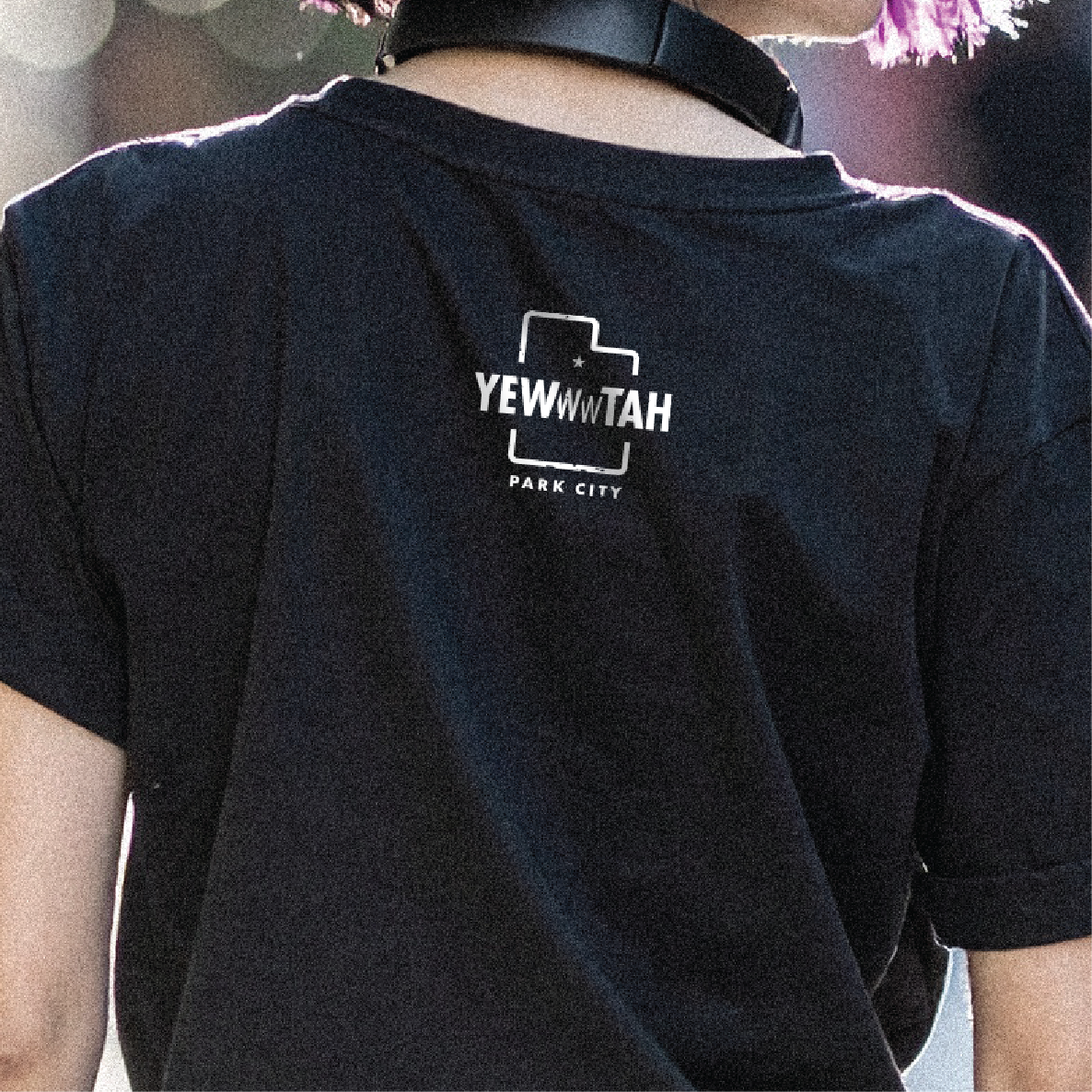 Black t-shirt with 'YEWWWTAH - PARK CITY' logo on the back, worn by a woman.