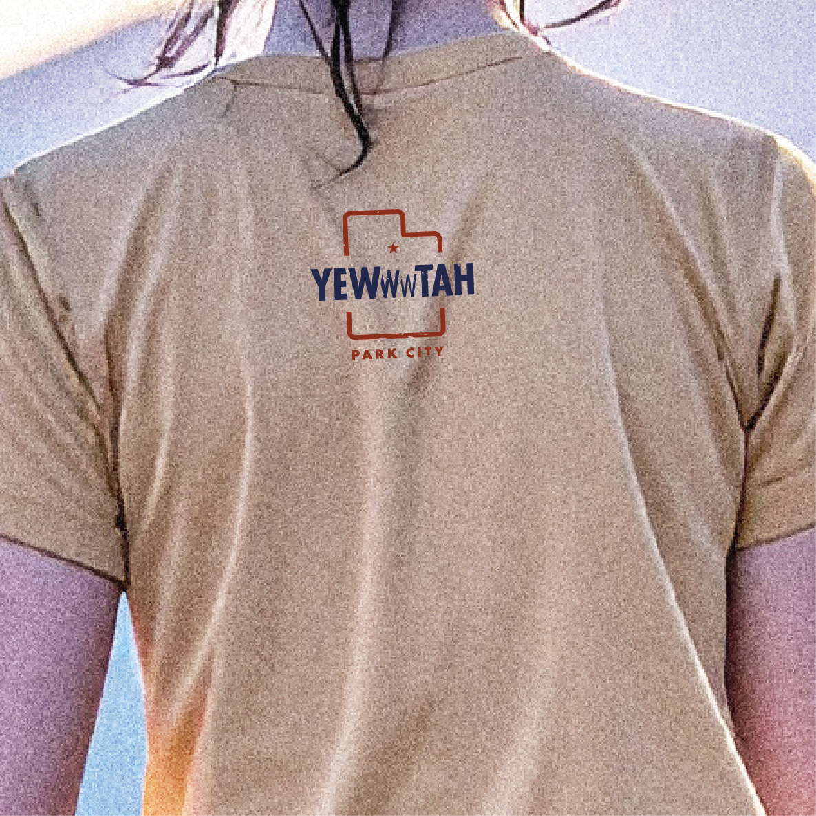 Beige t-shirt with 'YEWWWTAH' logo on a person against a blue sky.