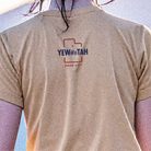 Beige t-shirt with 'YEWWWTAH' logo on a person against a blue sky.