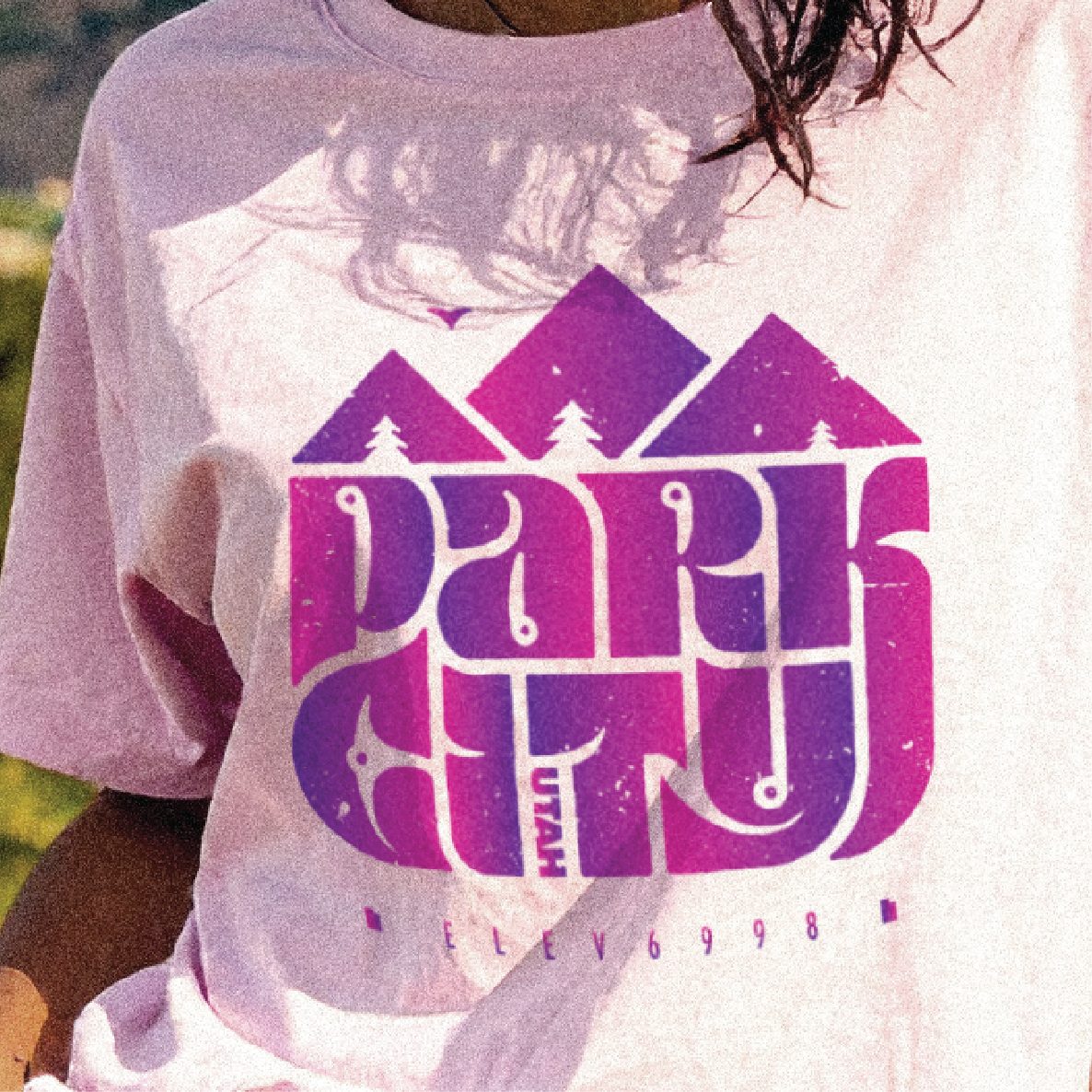 Person wearing a t-shirt with 'Park City Utah' design in purple and pink.