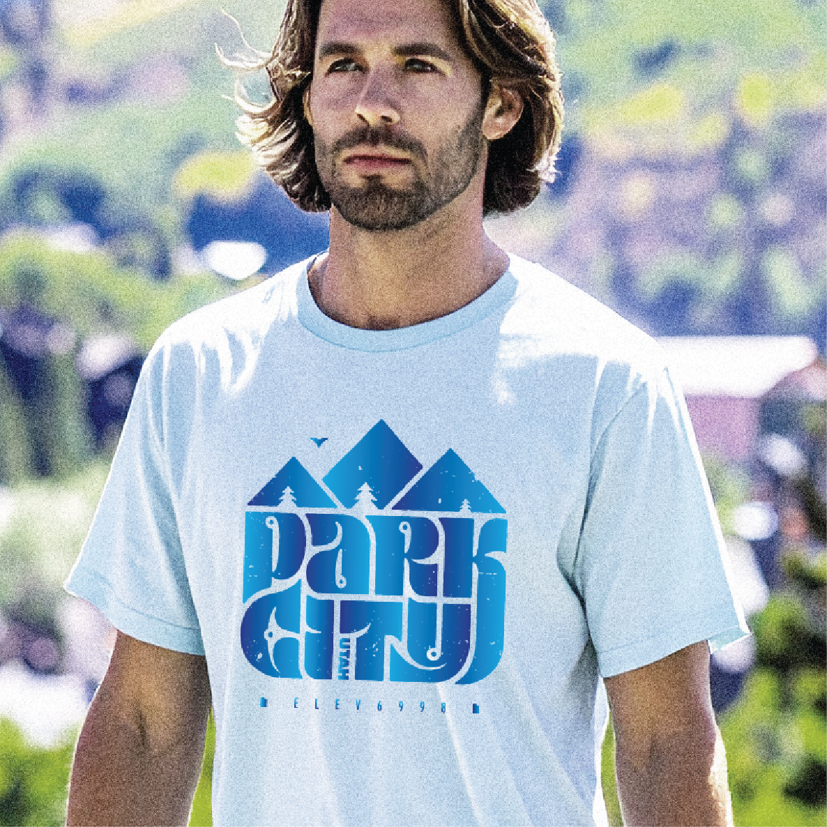 Man wearing a light blue t-shirt with a mountain graphic and Park City text outdoors.