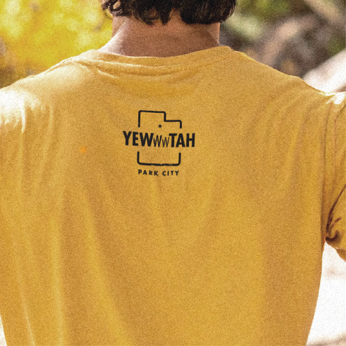 Yellow t-shirt with 'YEWWWTAH PARK CITY' logo on the back, worn by a person.