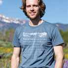 Man wearing a blue t-shirt with mountain design and text that says "Wasatch), standing outdoors with mountains in the background.