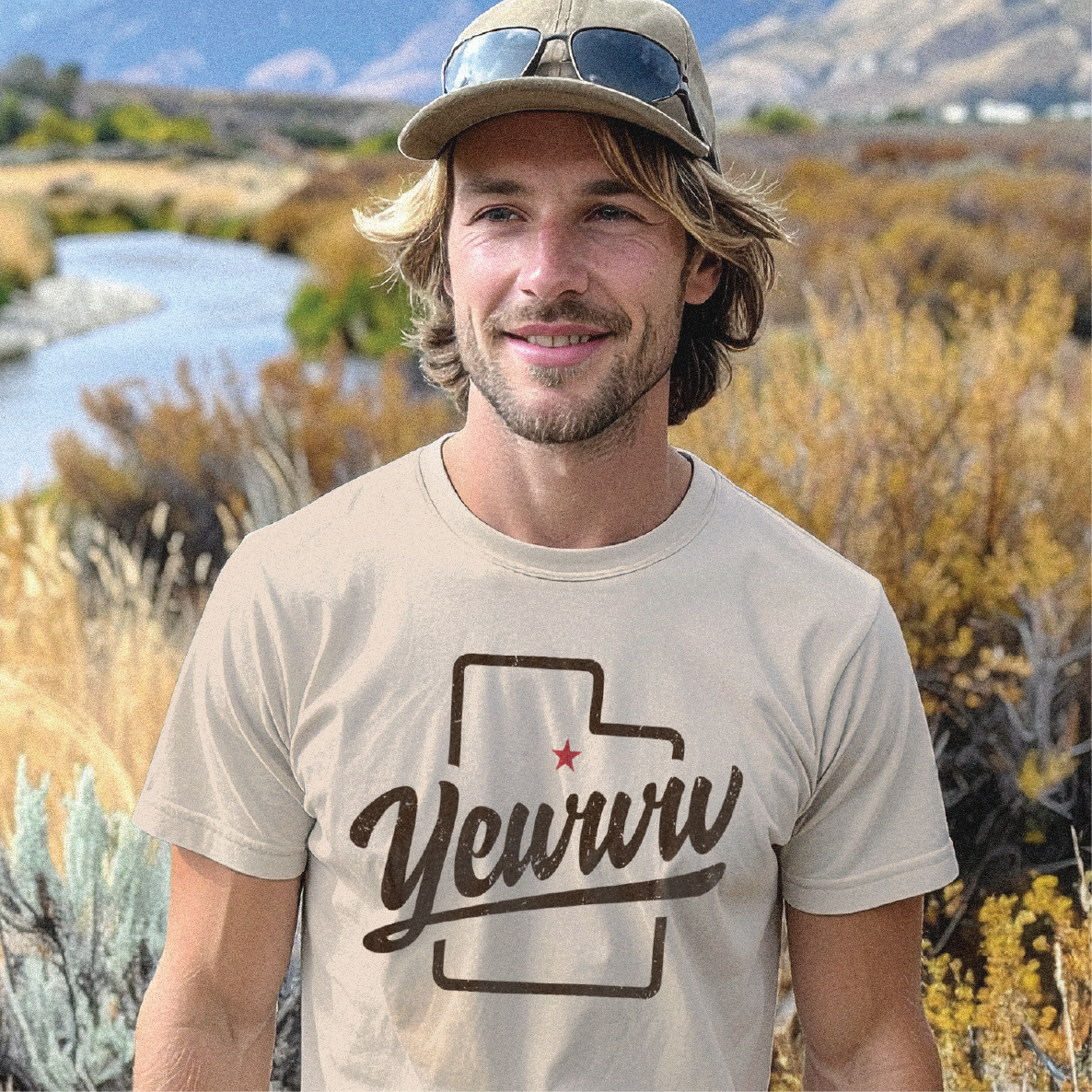 Man wearing a beige t-shirt with 'Yewww' design with an outlined shape of Utah in a natural setting with mountains and river.