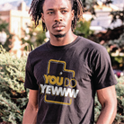 Person wearing a black t-shirt with a graphic design that reads 'you do yewww' outdoors